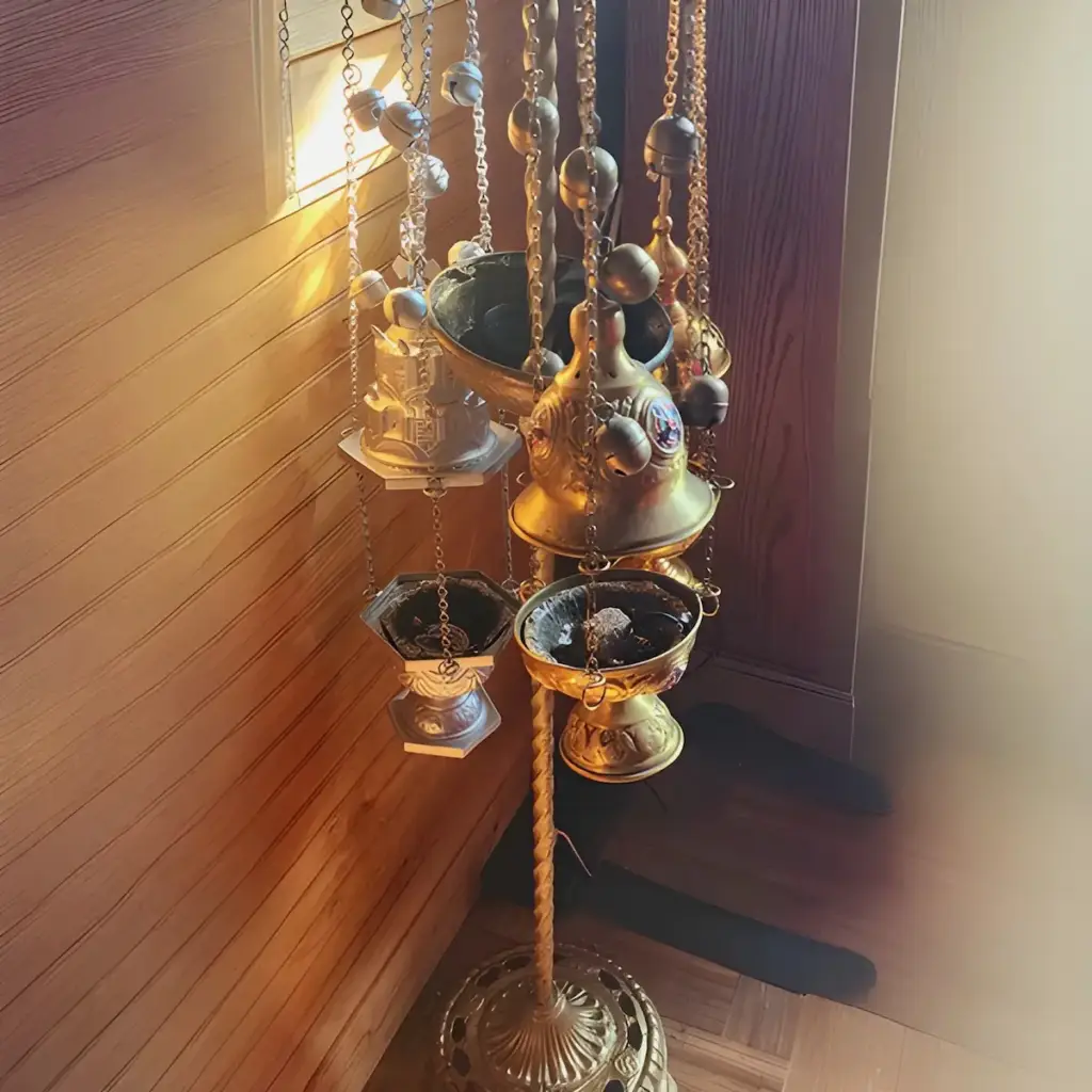 A close-up shot of a gold-painted censer with burning charcoal and incense. There are bells on the chains the censer is attached to.