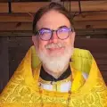 Father Gregory smiles and stands in the altar area in his vestments at Evangelist Luke Orthodox Mission Church.