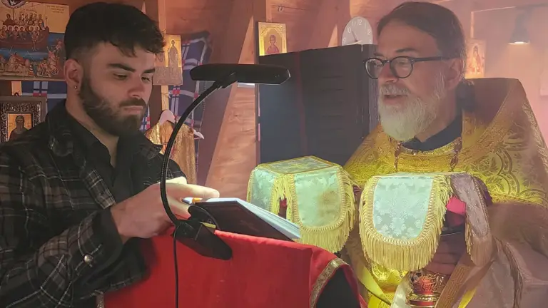 Evangelos the chanter holds a book for Father Gregory to read during a procession.