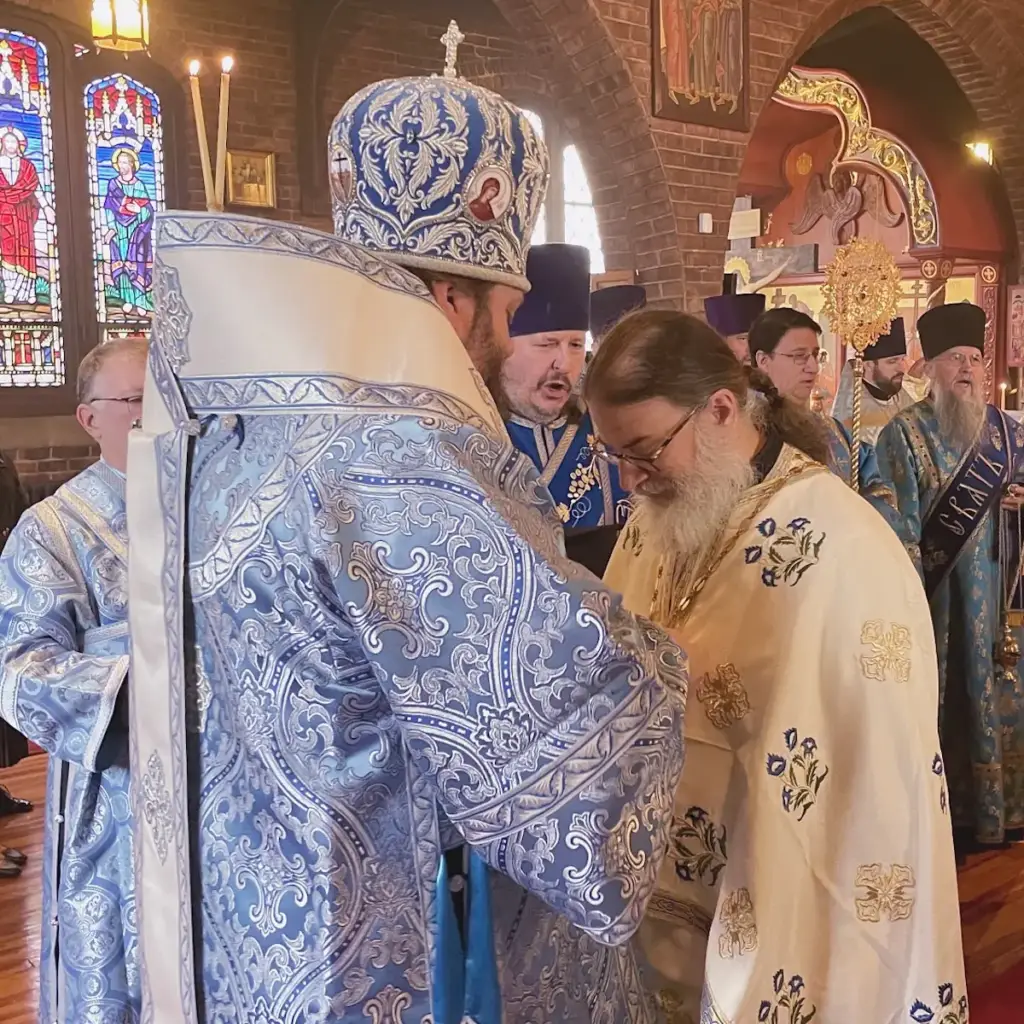A bishop is putting a gold cross on Father Gregory to welcome him into the church.