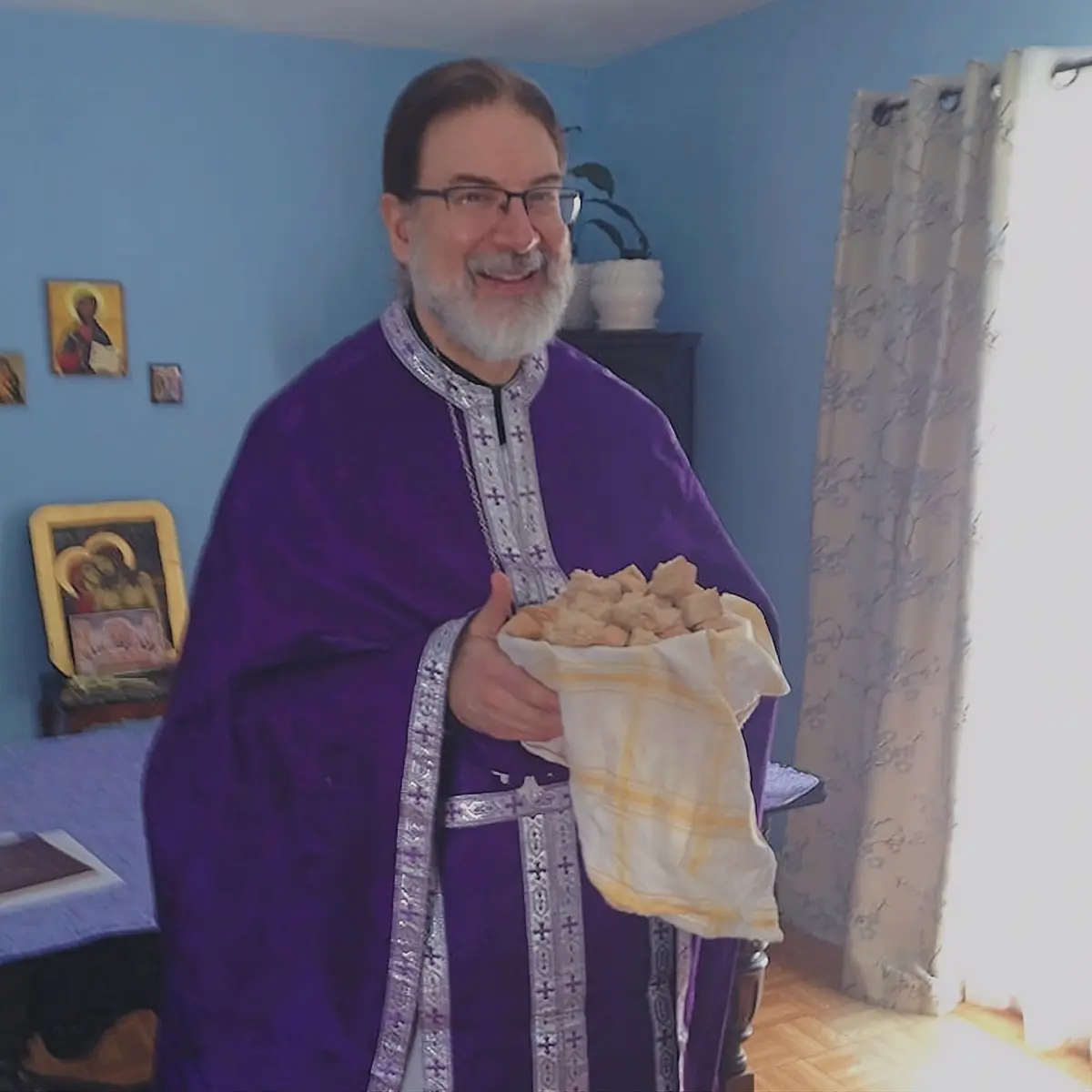Father Gregory smiling while holding the Holy Bread after a service.