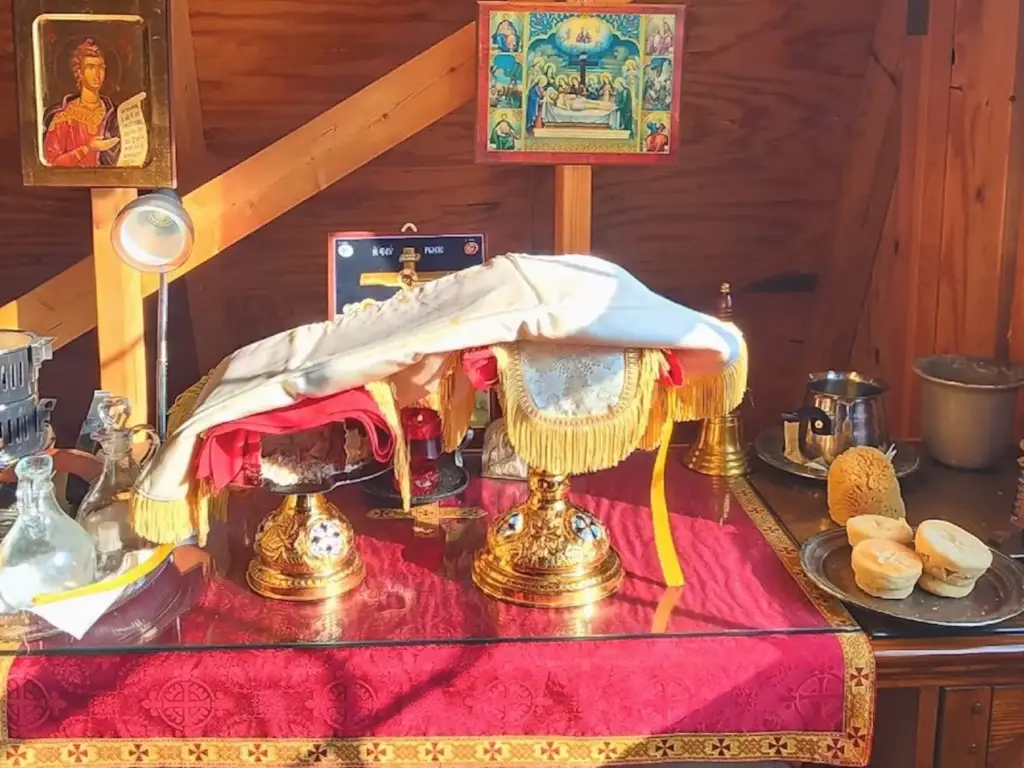 There are two chalices on a table, one holding the Holy Bread and the other containing Holy Communion. Surrounding the chalices are liturgical items.