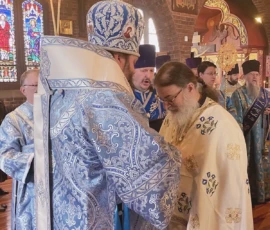 A bishop is putting a gold cross on Father Gregory to welcome him into the church.