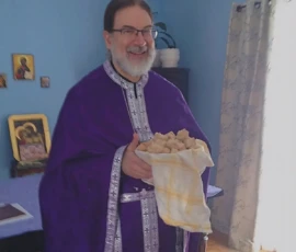 Father Gregory smiling while holding the Holy Bread after a service.