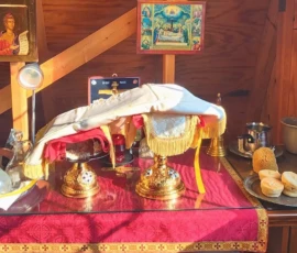 There are two chalices on a table, one holding the Holy Bread and the other containing Holy Communion. Surrounding the chalices are liturgical items.