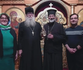 Clergy and faithful stand together before the iconostasis as a priest holds the cross during an Orthodox service inside the church.