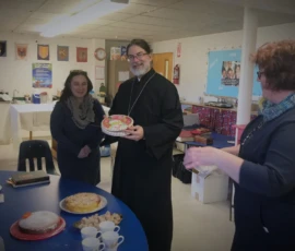 An Orthodox priest stands with parishioners inside the church following a service, with icons visible behind them.