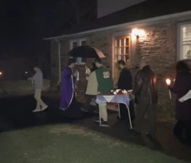 Clergy and parishioners walk together in prayer during a Holy Friday procession outside the church building at night.